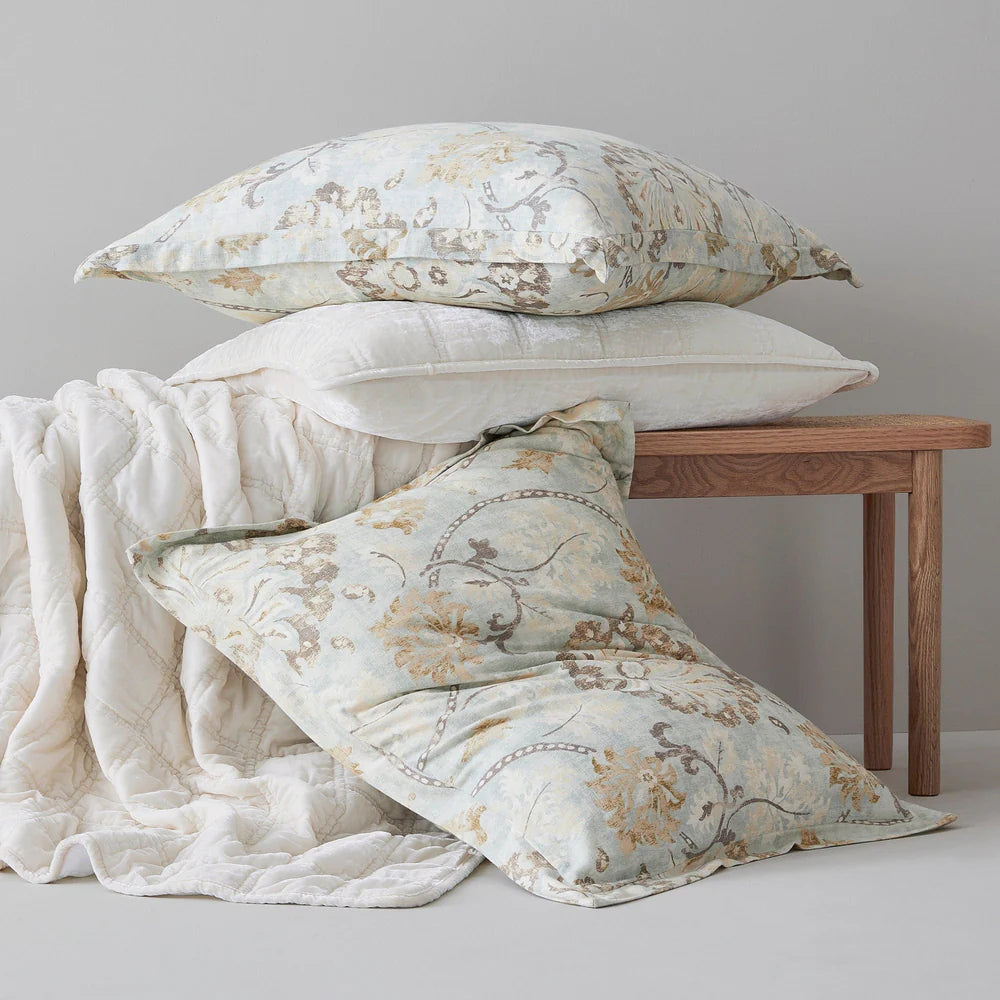 Decorative pillows with floral patterns on a wooden bench against a gray wall.