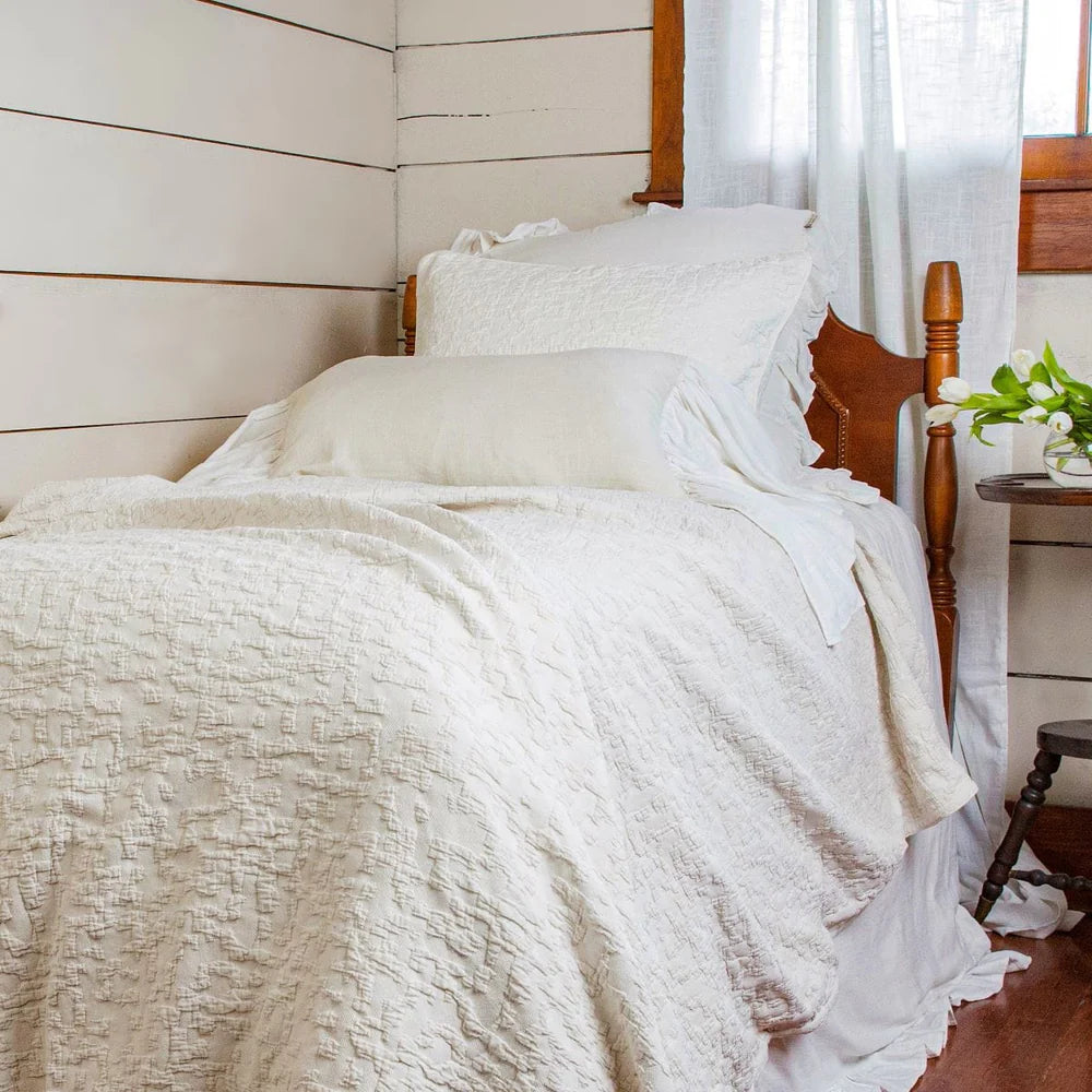 Bed with white bedding and pillows in a room with wooden walls and a window.