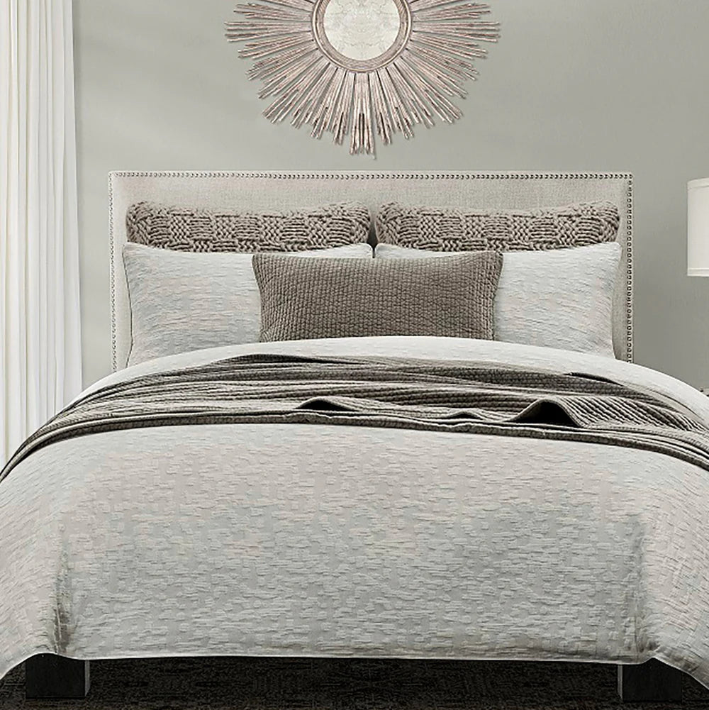 Neatly made bed with gray bedding and decorative pillows in a bedroom setting.