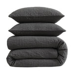 Stack of dark gray textured bedding including a duvet and two pillows on a white background
