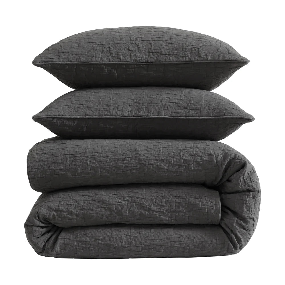 Stack of dark gray textured bedding including a duvet and two pillows on a white background