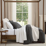 Four-poster bed with white bedding and gray throws in a bedroom setting.