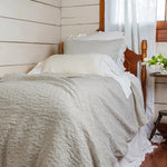 Bed with gray bedding and white pillows in a room with wooden walls and a window.