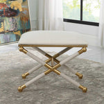 Decorative stool with gold legs and white cushion in a room with a painting and window.