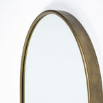 An oval-shaped full-length mirror with a gold antiqued metal frame.