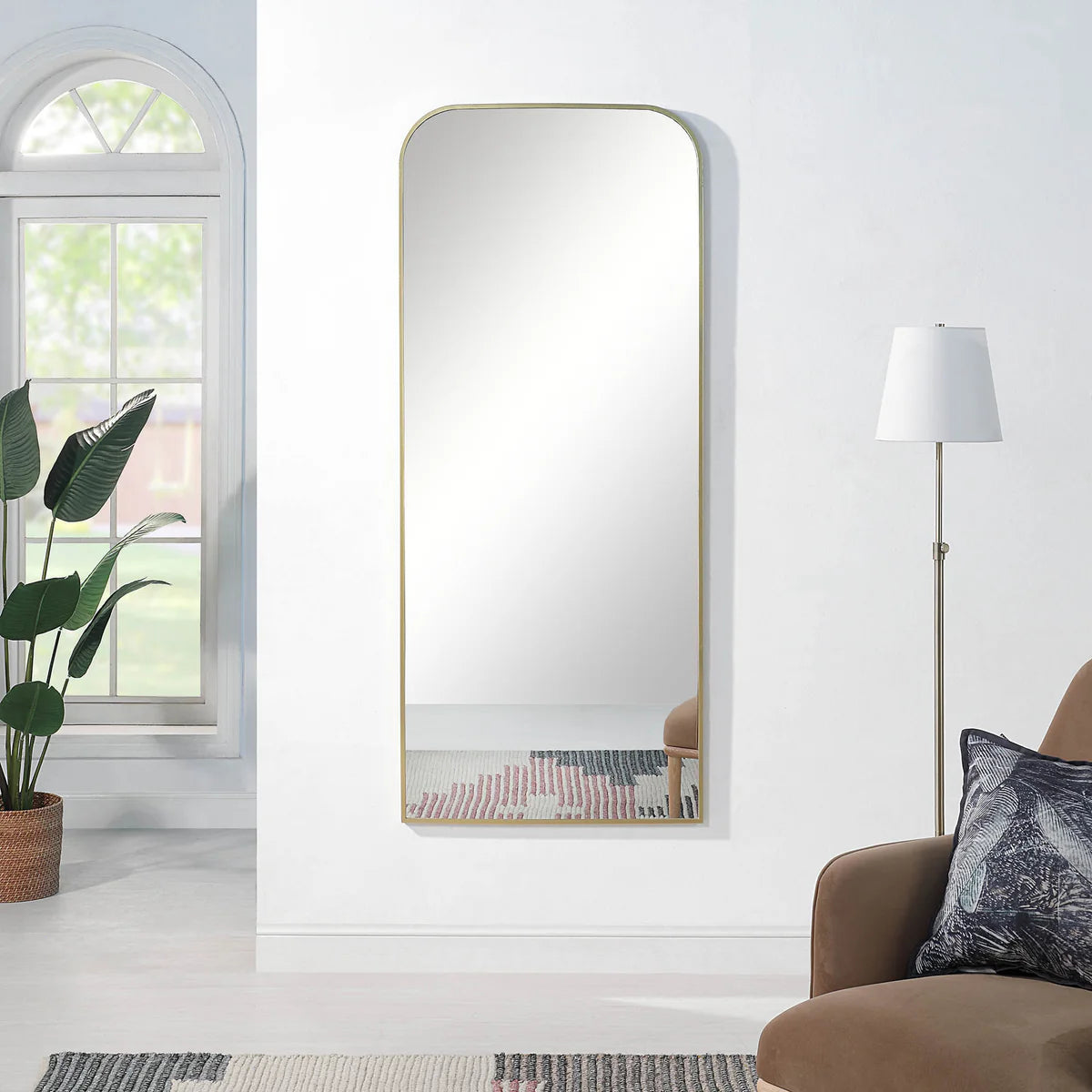 Full-length mirror with gold frame leaning against a white wall in a living room.