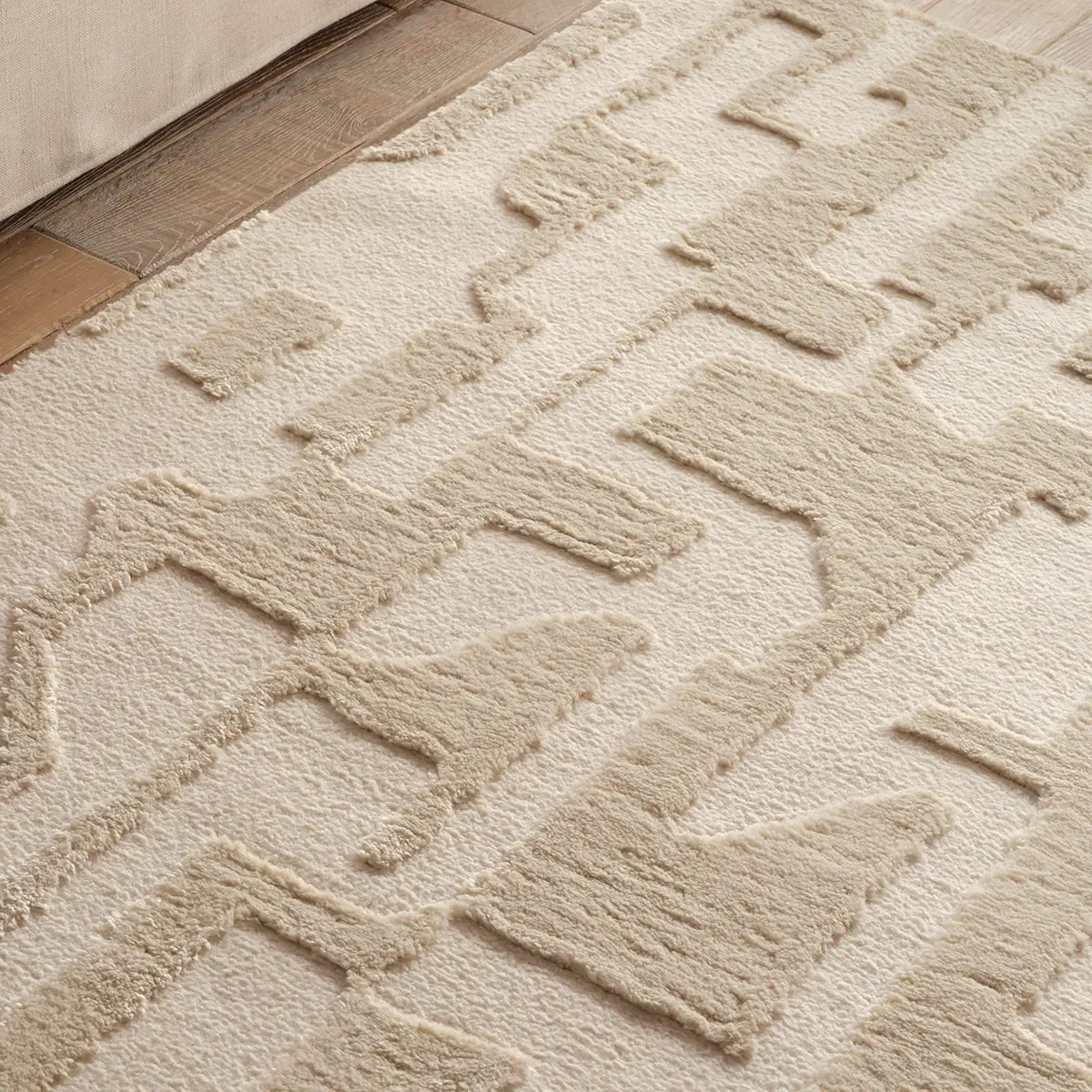 Close-up of a textured beige rug with geometric pattern on a wooden floor.