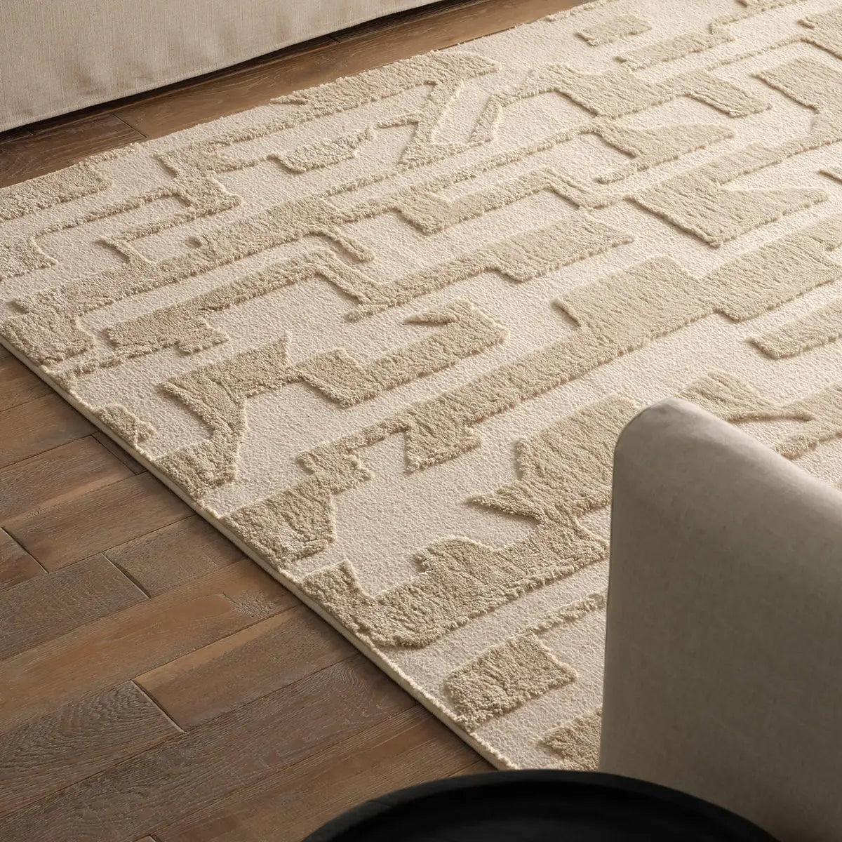 Beige textured rug on a wooden floor with a chair partially visible