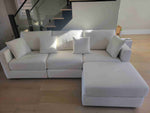A white Milford sectional sofa with four pieces, including cushions, in a room with hardwood flooring and a staircase in the background.
