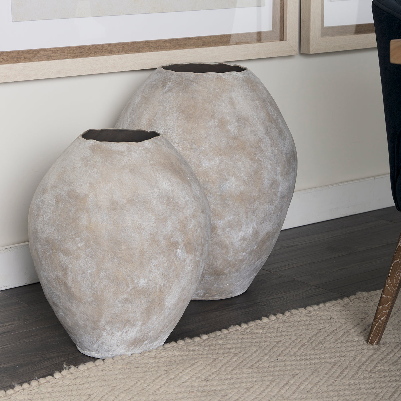 Two gray textured planters on a wooden floor with a neutral wall background.