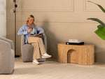 Woman reading a magazine in a modern living room with a wooden side table.