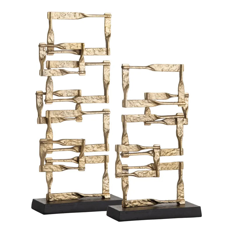 A set of two gold-colored metal decorative objects with a geometric design, placed on a dark base.