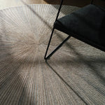 Round textured rug with a chair casting a shadow on it