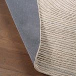 Close-up of a gray and beige textured rug on wooden flooring.
