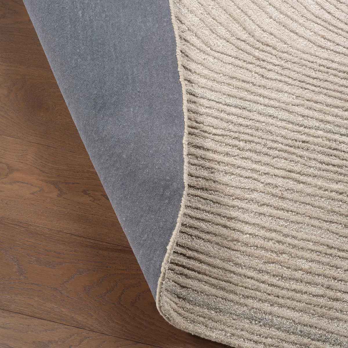Close-up of a gray and beige textured rug on wooden flooring.