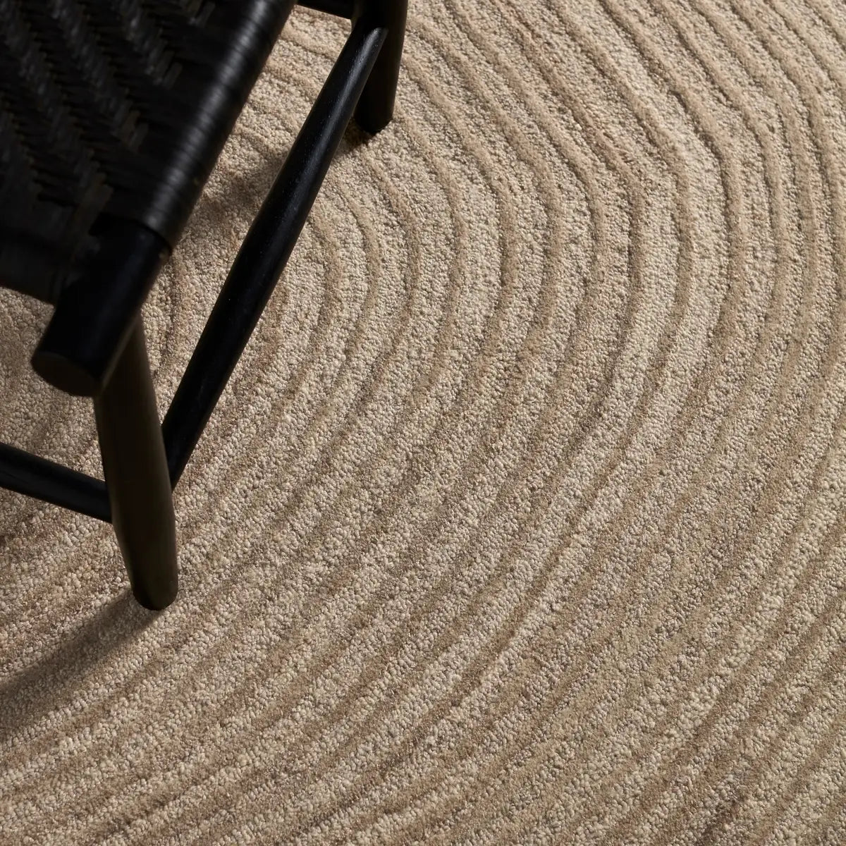 Close-up of textured beige carpet with a black chair leg visible
