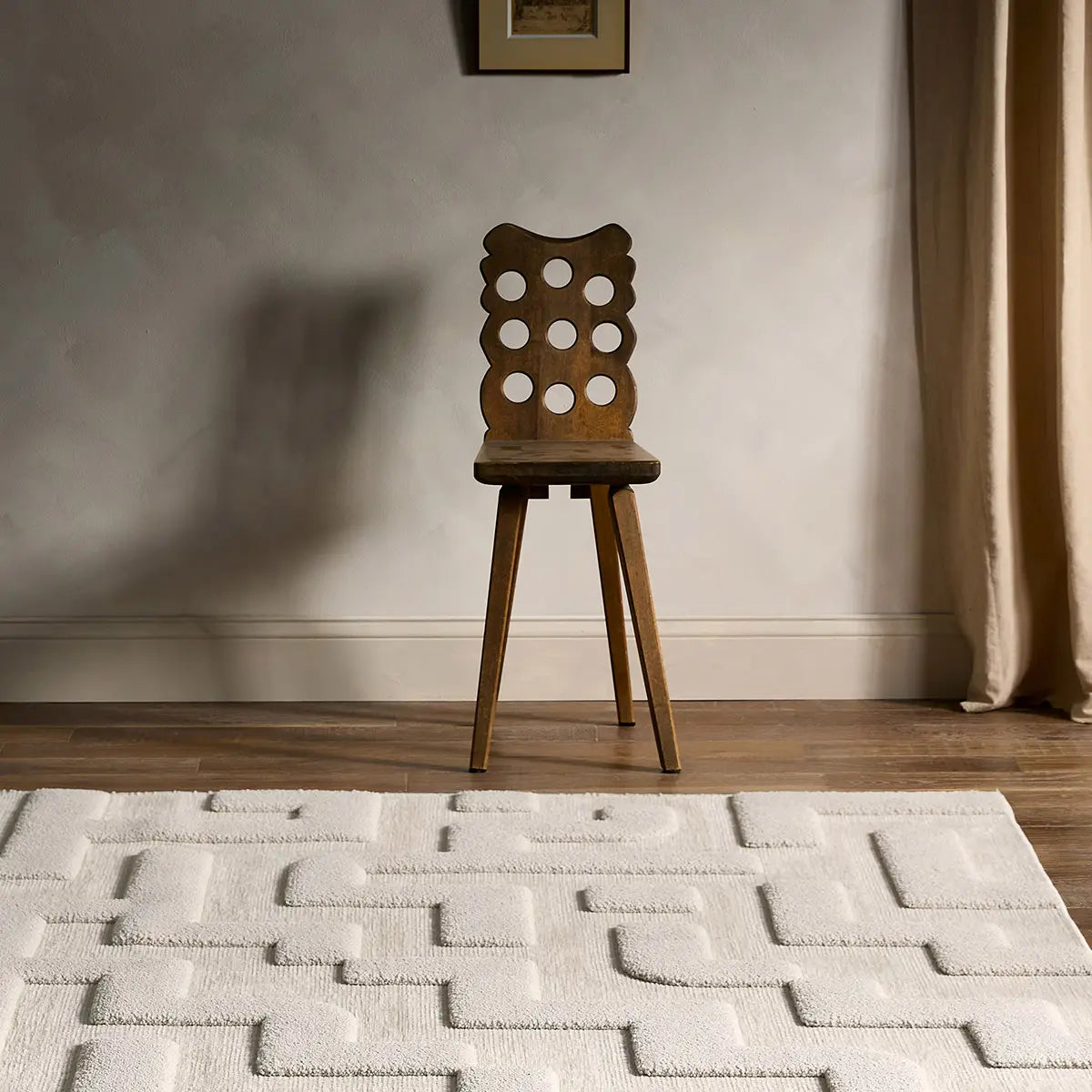 Wooden chair on a textured rug with a neutral wall and curtain in the background
