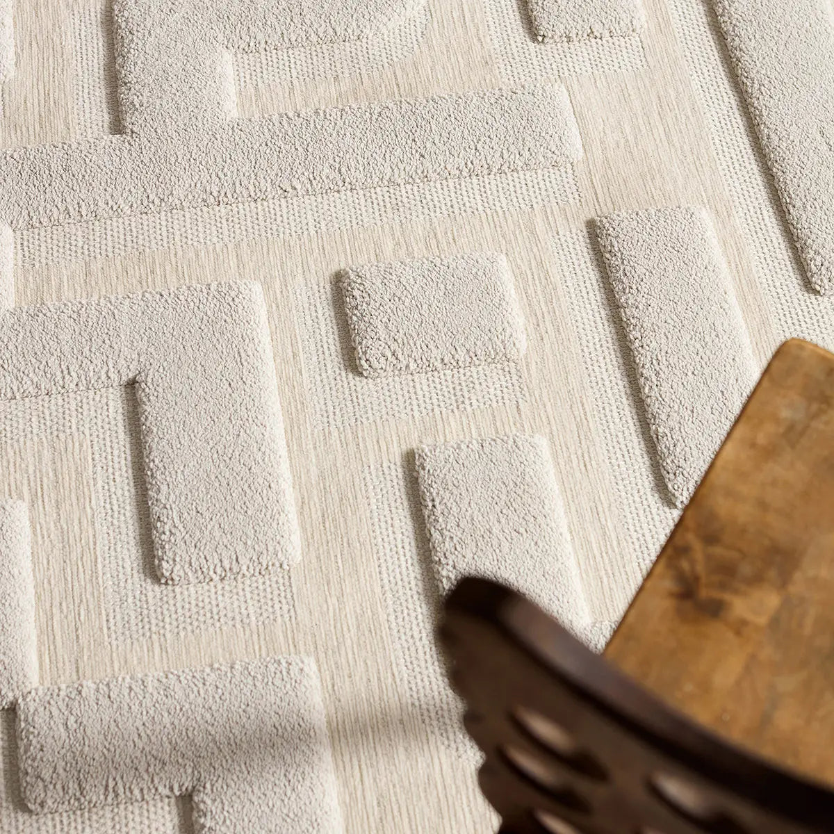 Textured beige rug with geometric pattern next to a wooden chair