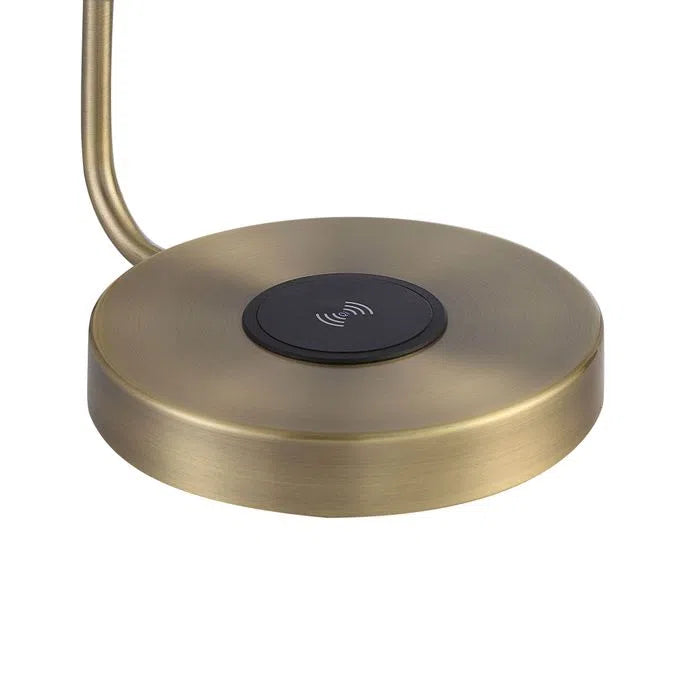 A table lamp with a brass finish, featuring a sleek, modern design with a rounded shade and a flat base with charging pad