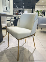 A modern dining chair with a white upholstered seat and backrest, featuring gold-colored metal legs.