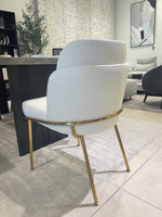 A modern dining chair with a white upholstered seat and backrest, featuring gold-colored metal legs.