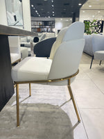 A modern dining chair with a white upholstered seat and backrest, featuring gold-colored metal legs.