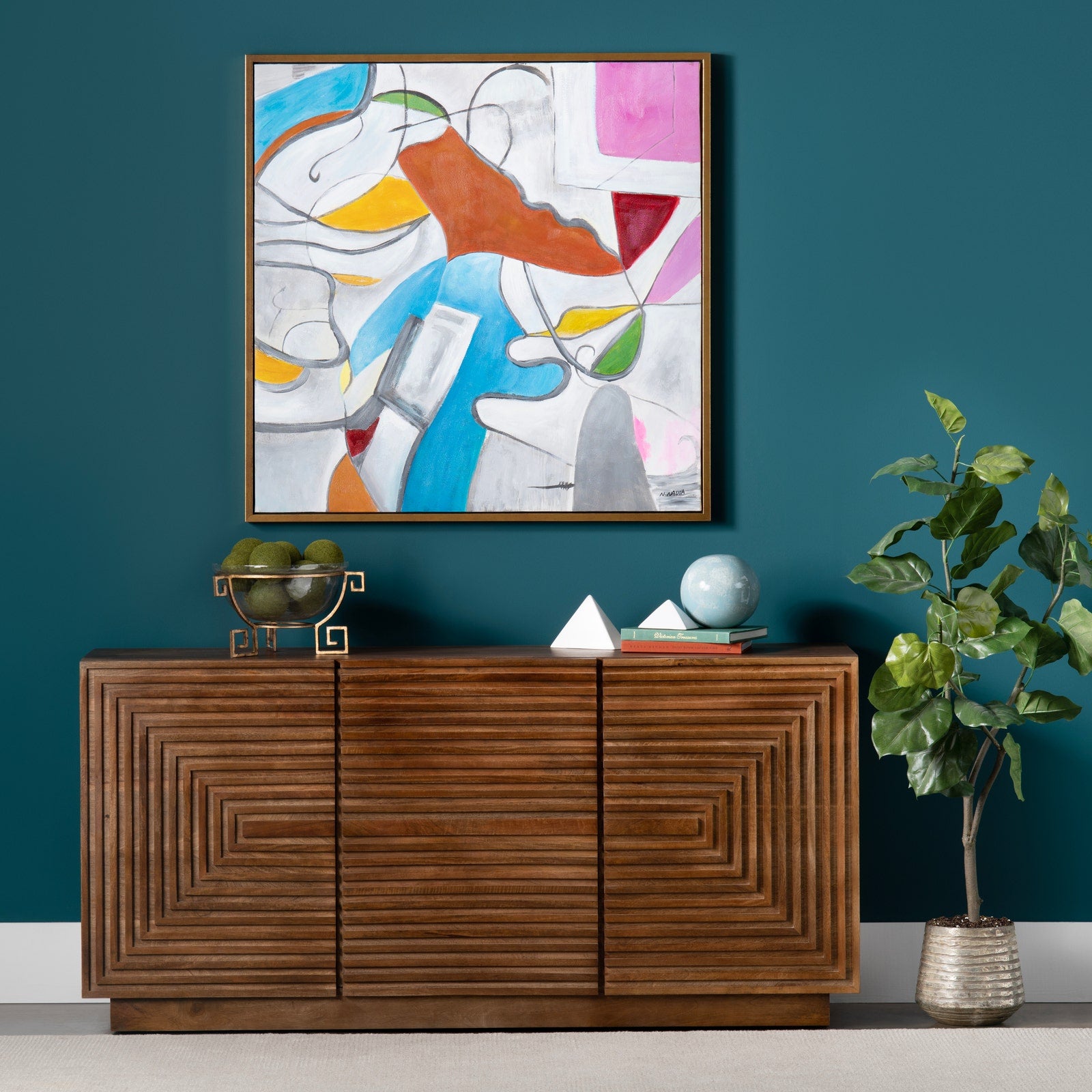 Wooden sideboard with decorative items against a teal wall with a colorful abstract painting.
