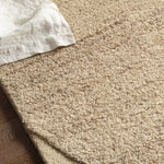 Beige carpet with a corner of a white pillow and wooden floor.