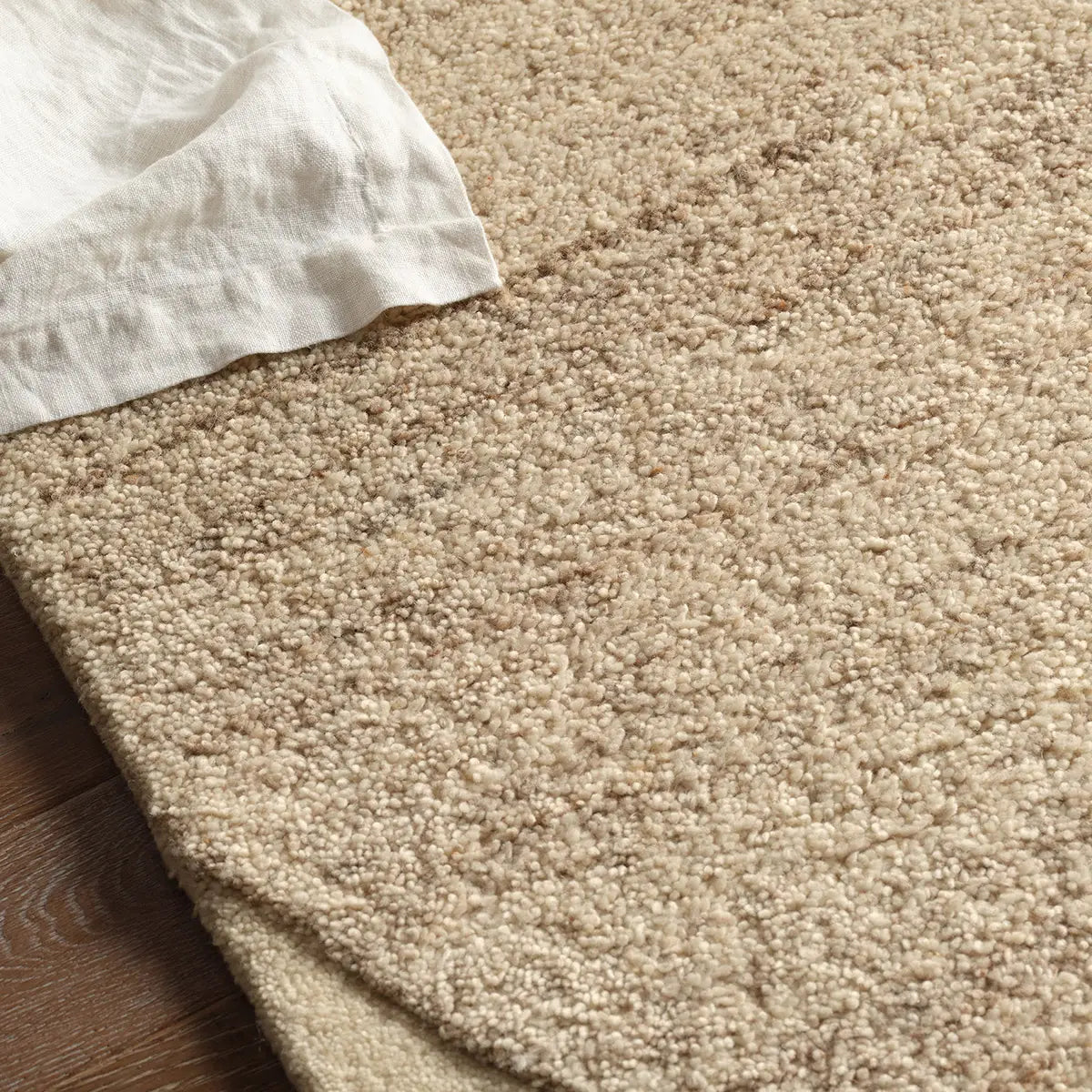 Beige carpet with a corner of a white pillow and wooden floor.
