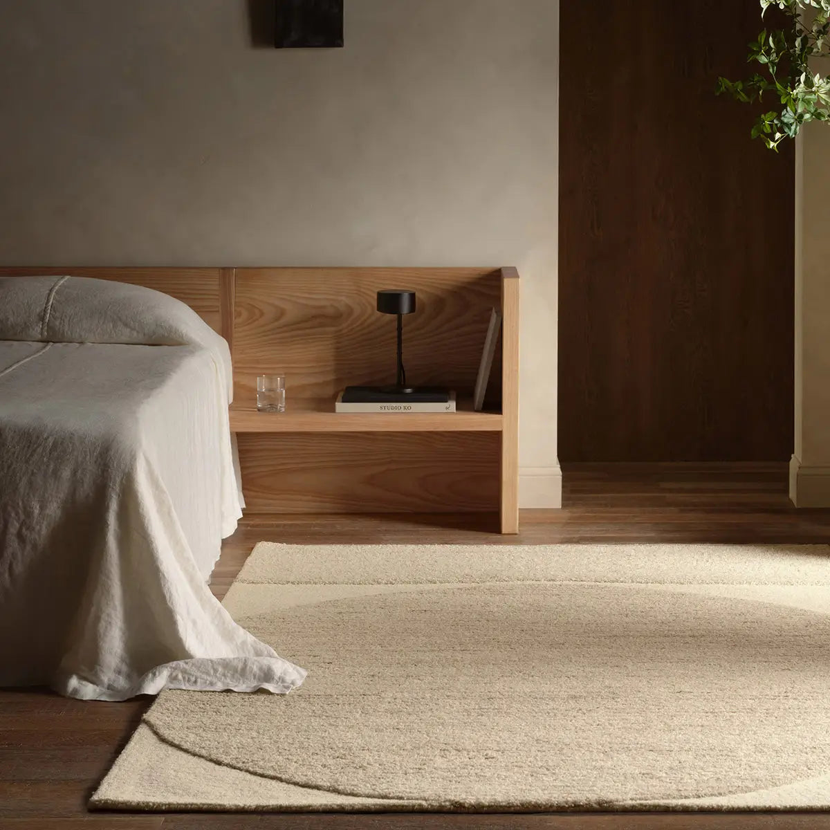 Bedroom with wooden headboard and nightstand, beige rug on wooden floor.