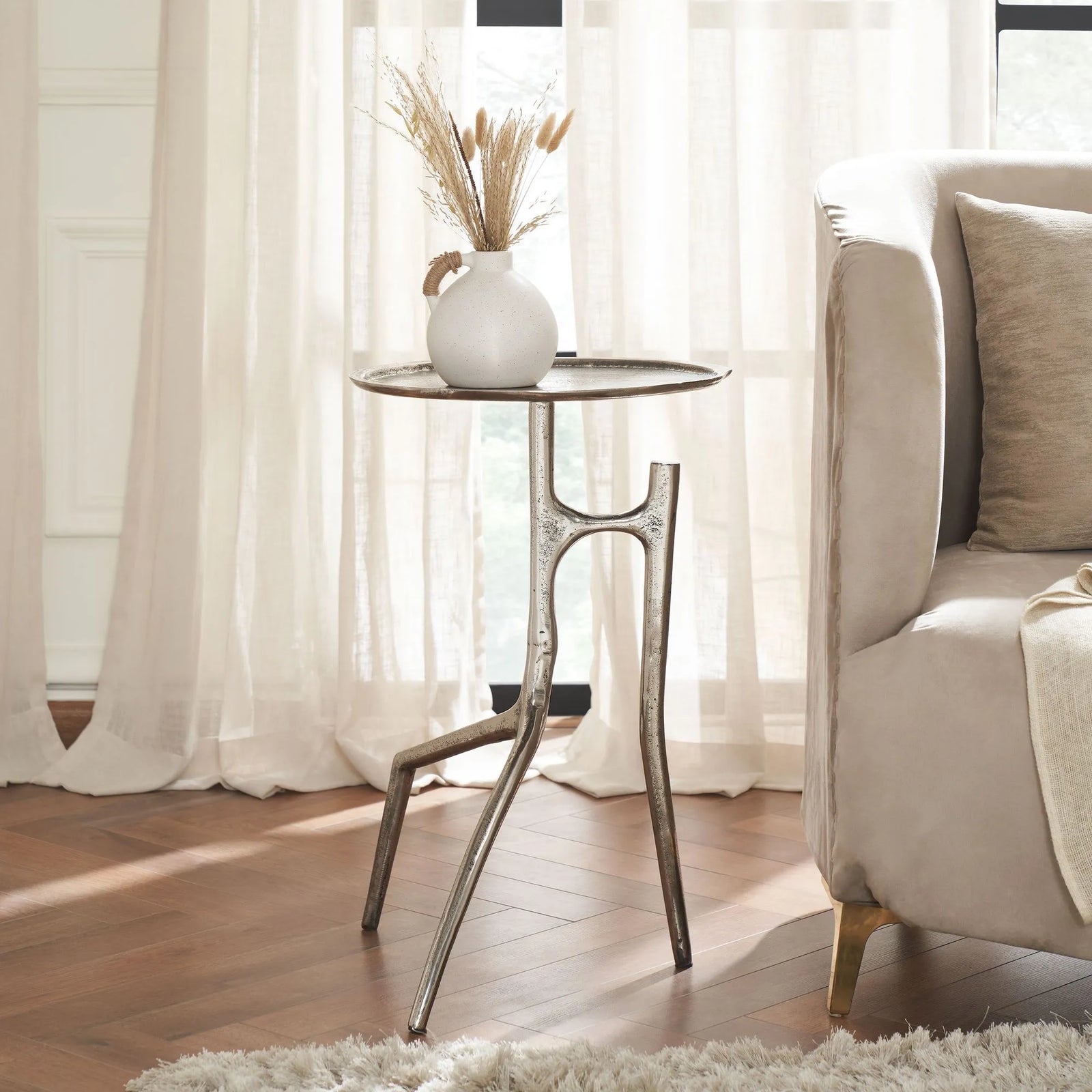 Small round table with decorative vase next to a beige sofa in a bright room.