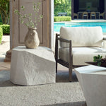 Outdoor setting with a stone table, vase with plants, and patio furniture near a pool.