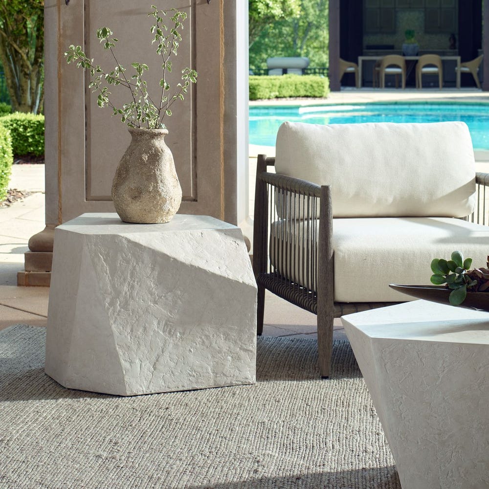 Outdoor setting with a stone table, vase with plants, and patio furniture near a pool.