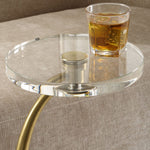 Glass side table with a gold leg holding a glass of amber liquid on a textured surface.