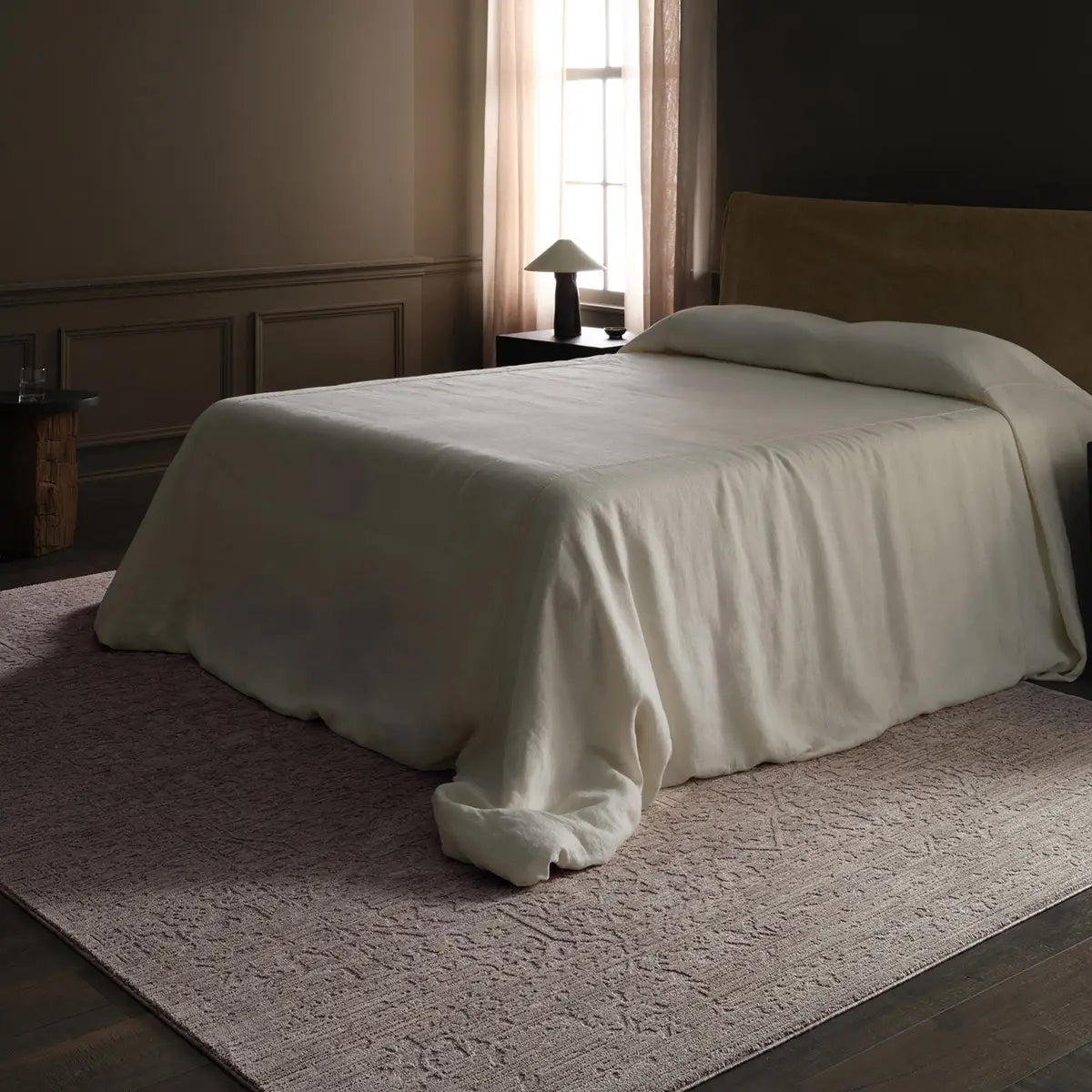 Bed with a beige blanket in a dimly lit bedroom