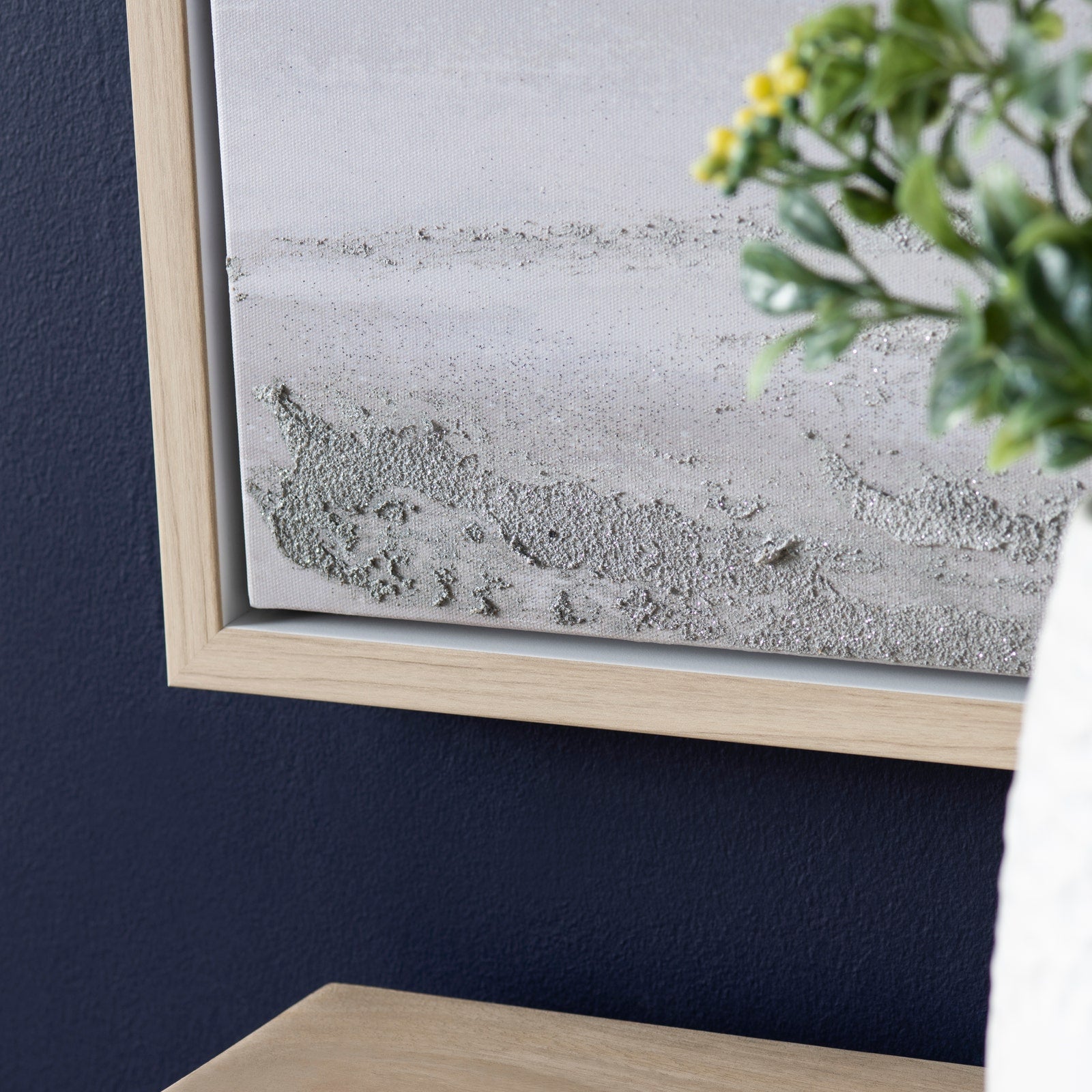 Framed concrete wall art on a dark blue wall with a plant in the corner.