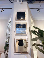 Set of three decorative mirrors on a white wall with a plant and shelf in the foreground.