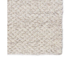 A beige, solid color wool area rug handwoven with a visible texture.