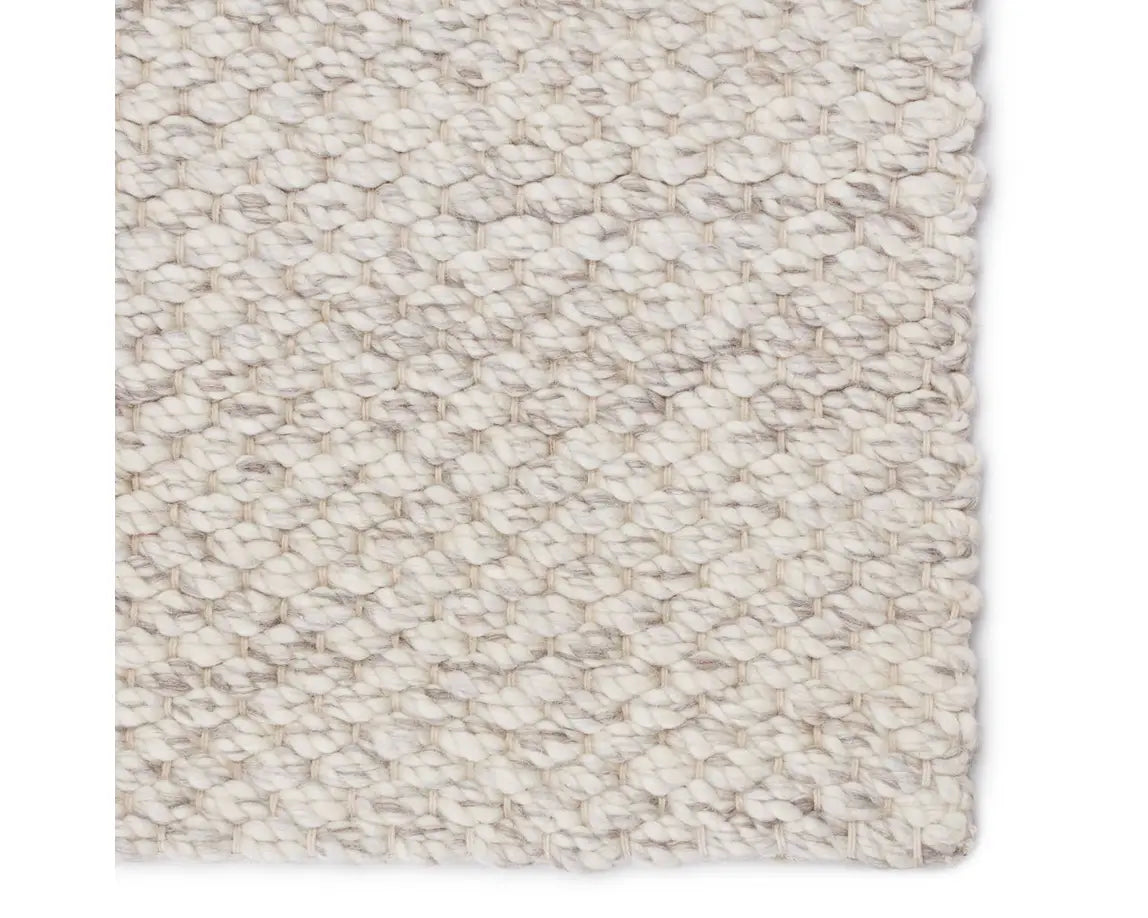 A beige, solid color wool area rug handwoven with a visible texture.