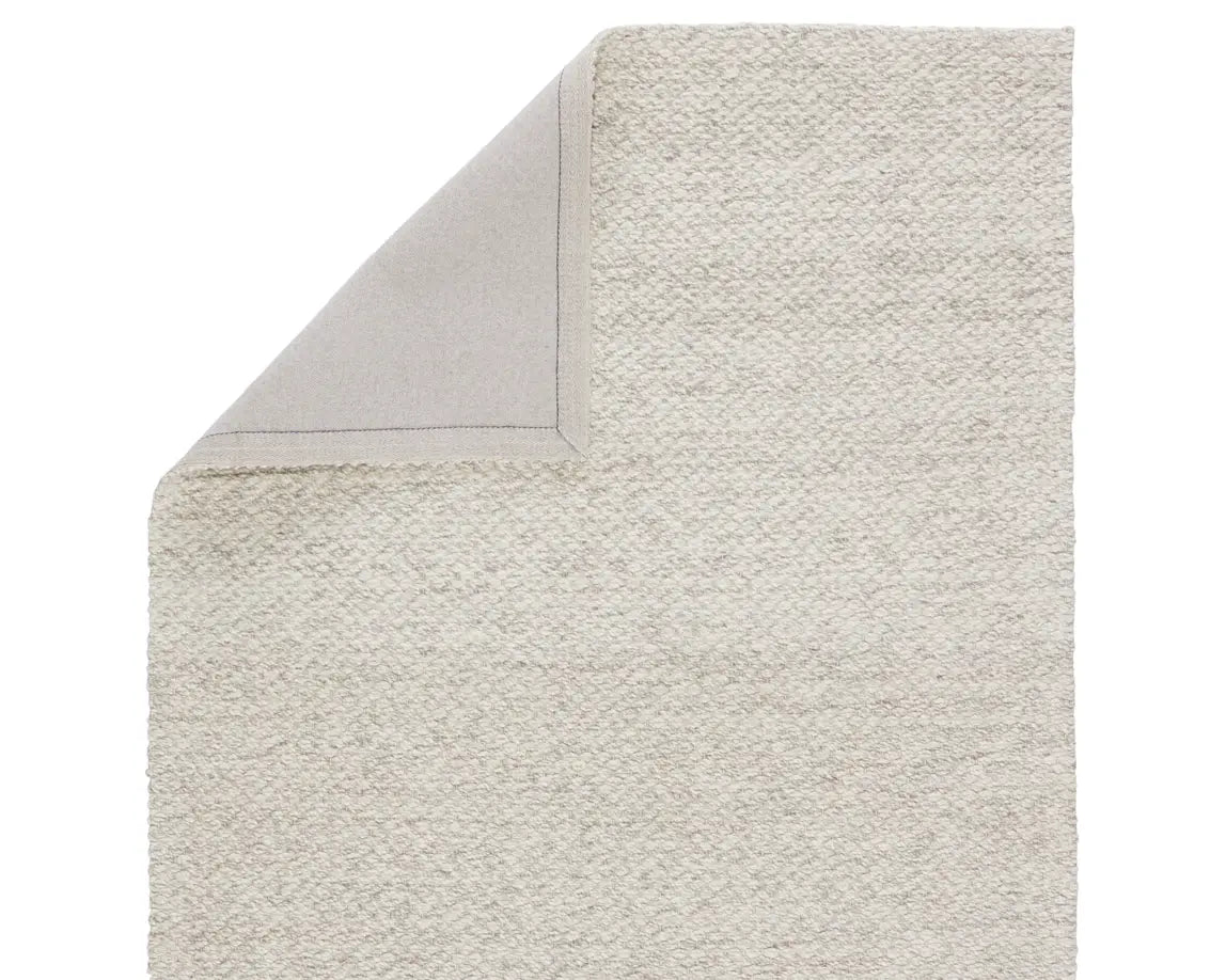 A beige, solid color wool area rug handwoven with a visible texture.