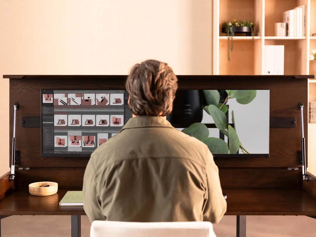 Person sitting at a desk with a computer setup, looking at a screen displaying images.