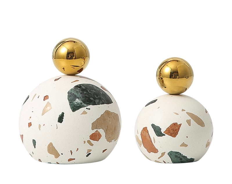 Two decorative terrazzo objects with a white base color and a gold-colored sphere on top, varying in size.