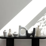 Collection of ceramic vases on a black table with a geometric light pattern on the wall.