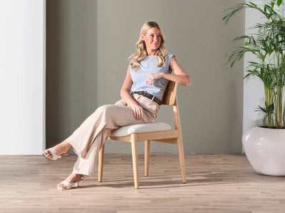 Woman sitting on a chair in a modern room with a plant and neutral decor.