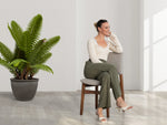 Woman sitting on a chair next to a potted plant in a bright room.