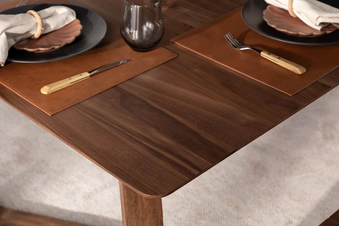 Wooden dining table with placemats, plates, and cutlery on a neutral background