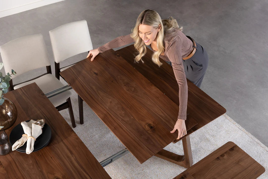 Woman adjusting a wooden dining table in a modern kitchen.