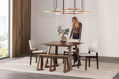 Dining room with wooden table, chairs, and a woman standing near the table.