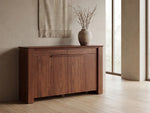 Wooden sideboard with a vase of branches in a room with large windows.