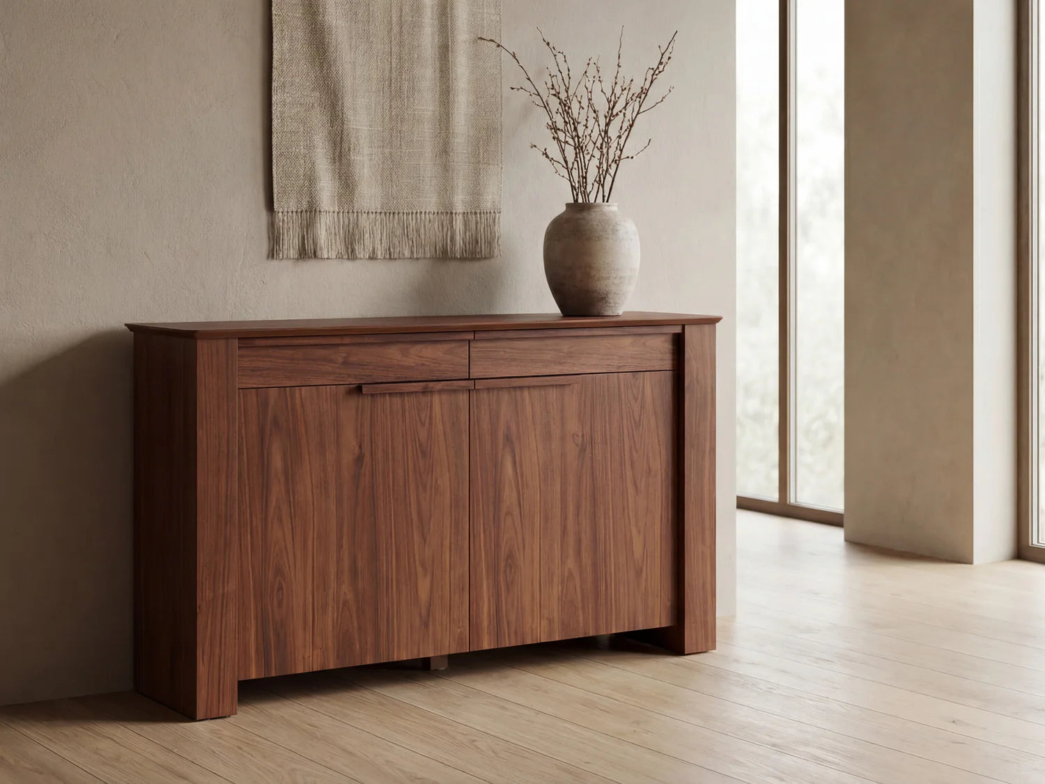Wooden sideboard with a vase of branches in a room with large windows.